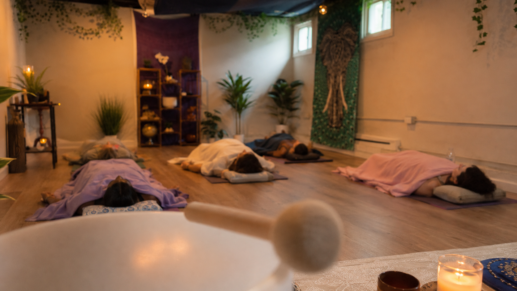 Five participants resting during a Guided Grounding sound bath viewed from behind the singing bowls